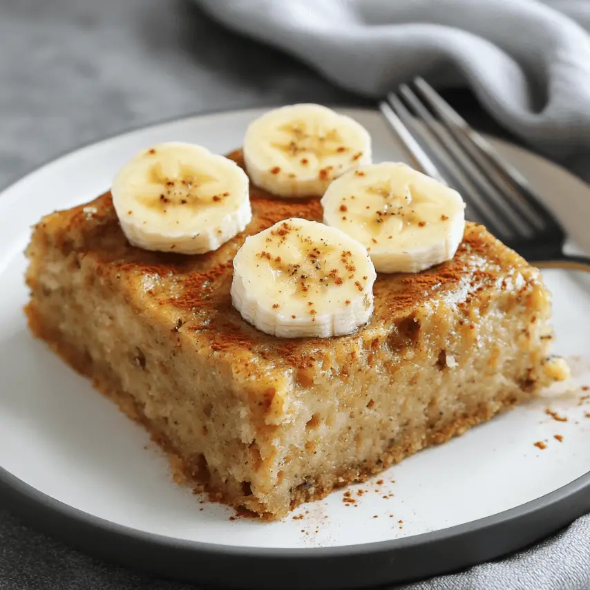 Part de gâteau moelleux à la banane, sans farine, sans sucre ajouté ni lait, servie sur une assiette en céramique avec une cuillère en bois.